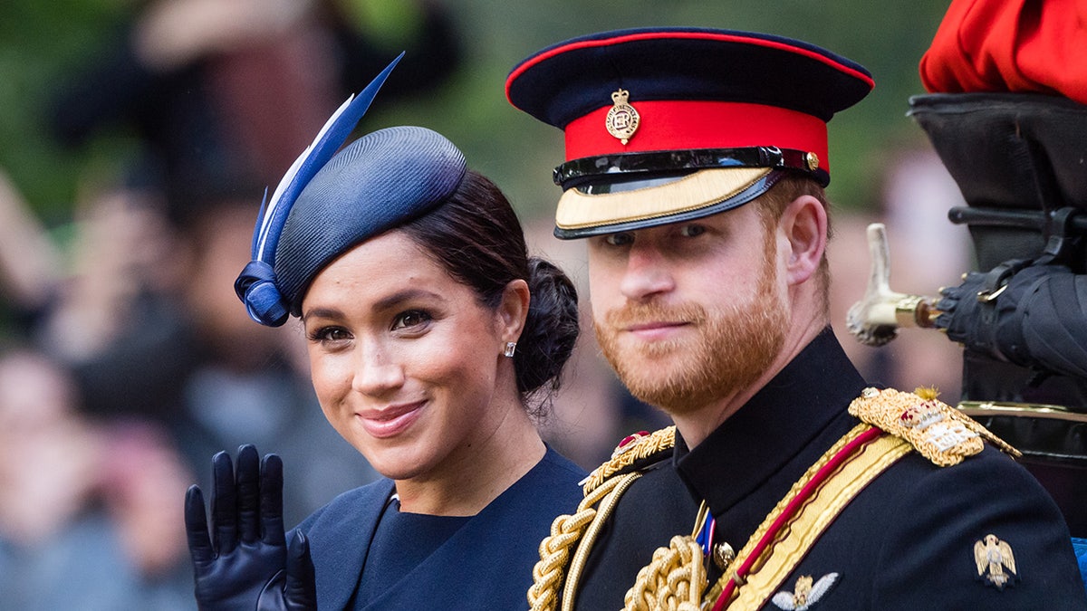 Meghan Markle and Prince Harry in formal wear smiling and waving to a crowd from a carriage.