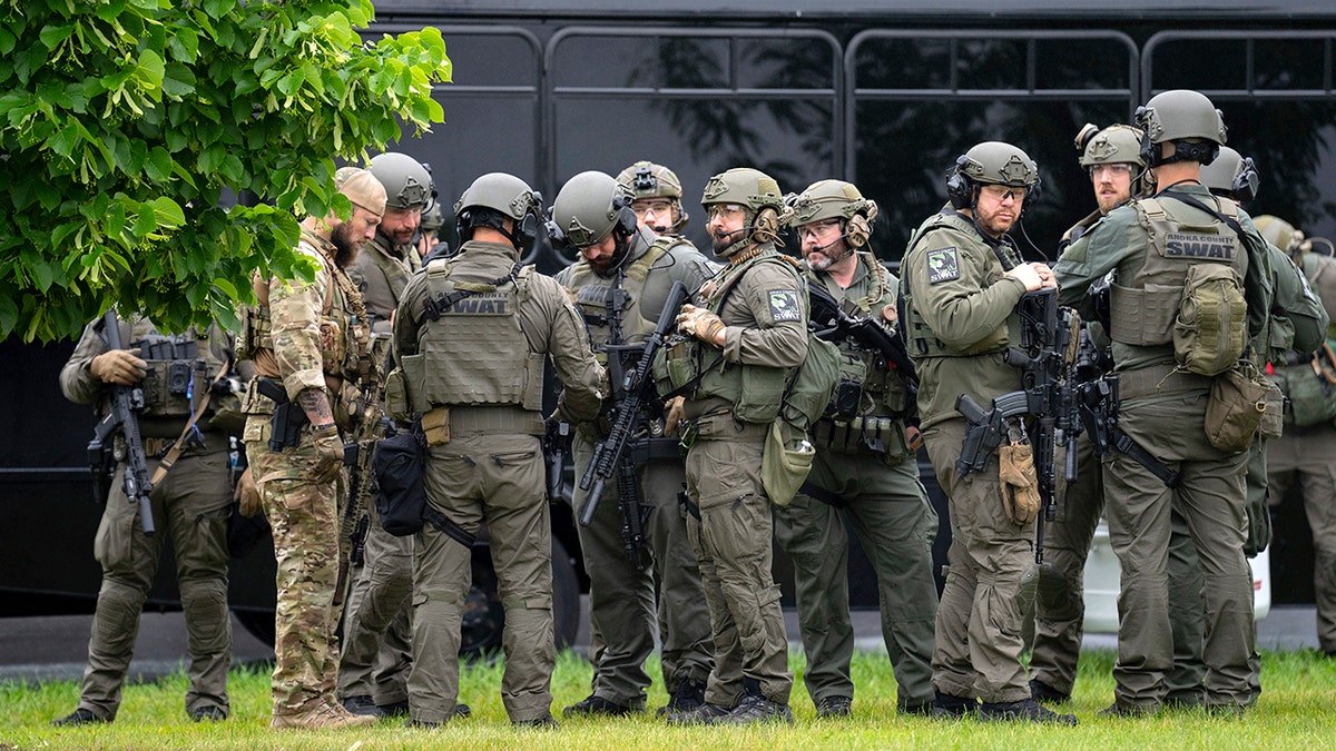 Law enforcement on a lawn with a bus in the background