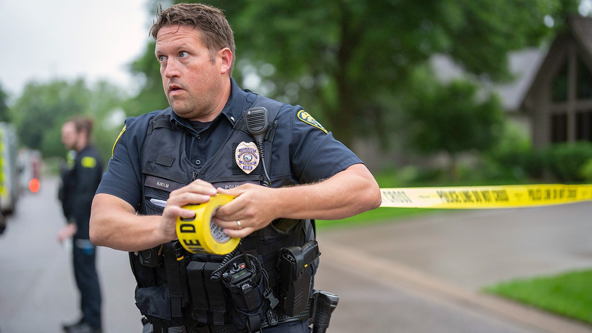 A police officer with crime scene tape in front of a house