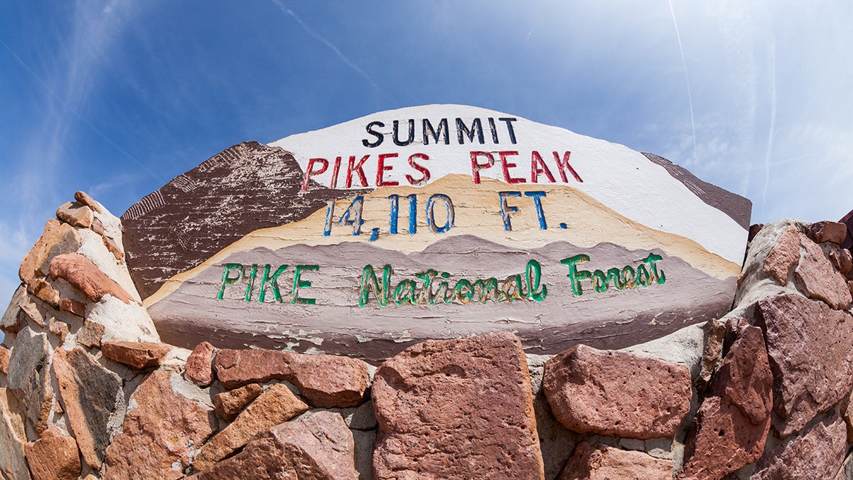 Sign plate for the summit of Pikes Peak resting atop red rocks