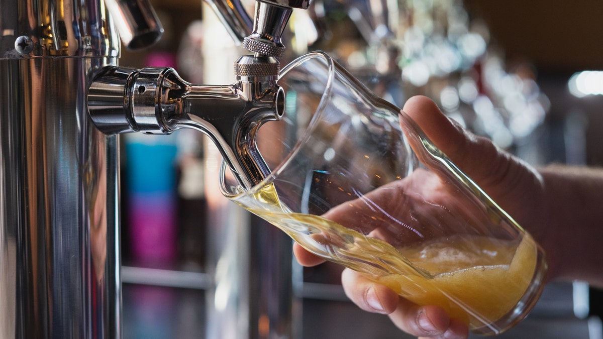 A hand holds a glass as cider is poured from a tap.