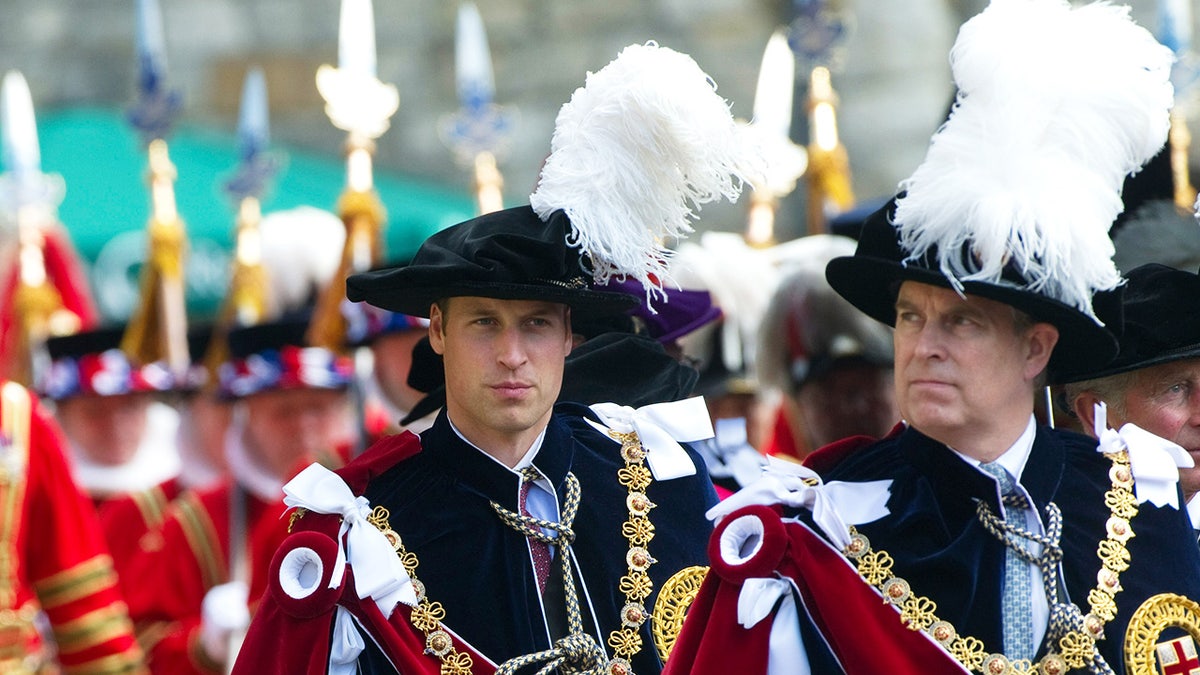 Prince William and Prince Andrew walk along the Royal Robes, looking serious.