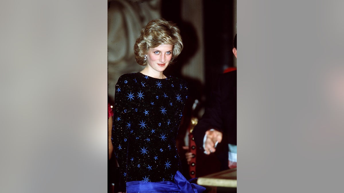 Princess Diana smirking in a black and blue dress with blue stars.