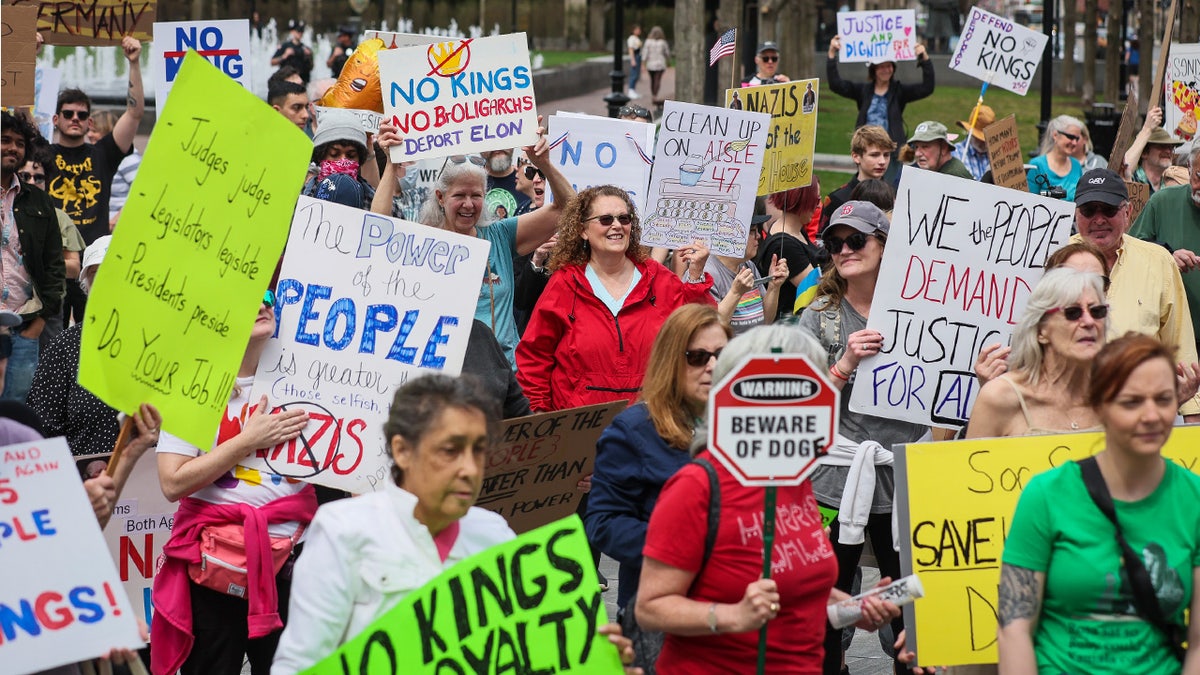 Demonstrators hold various signs including "The Power of the People" and "No Kings No Royalty"