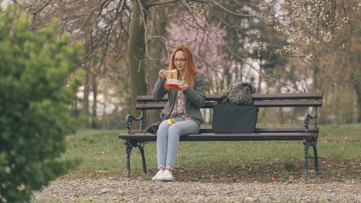 Woman eating noodles on bench