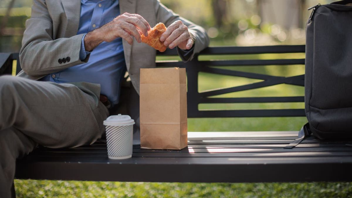 Close-up of man eating croissant on bench