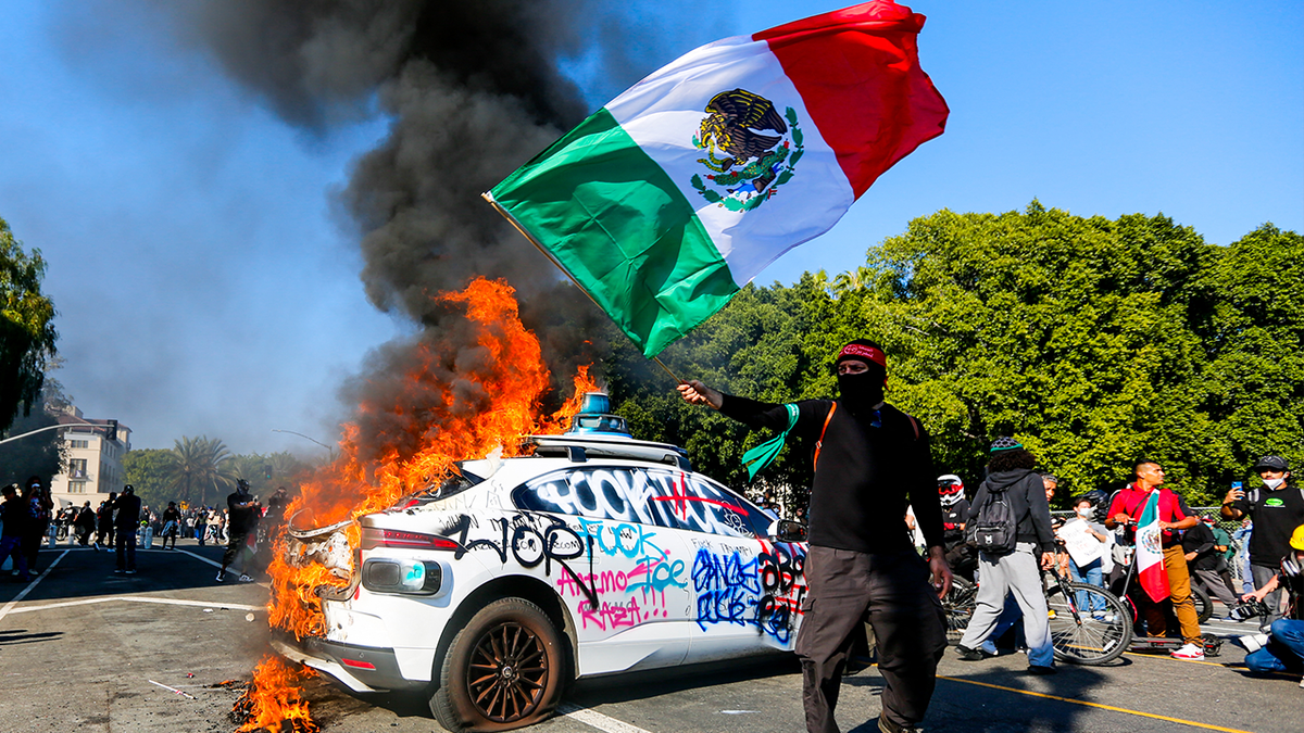 burning car as protester waves Mexican flag