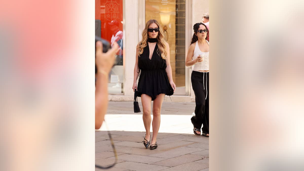 Sydney Sweeney in a black dress and sunglasses walking down the street in Venice