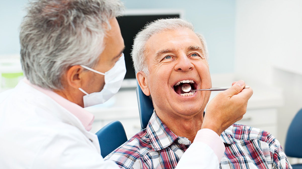 A senior man from the dentist gets his teeth considered as a dental mirror, put in his mouth, and he looks forward while sitting in his chair