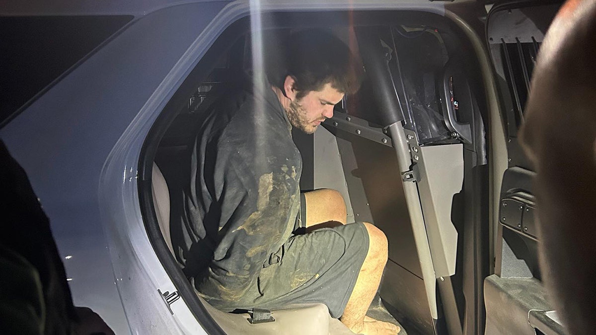 Trevor McEuen barefoot and handcuffed in the back of a cop car