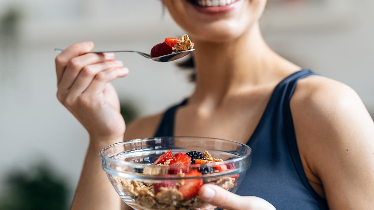 A woman smiles while holding a spoon with cereals and high fiber berries.
