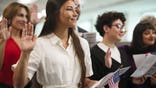 A diverse group of people in a ceremony taking the United States Naturalization Oath of Allegiance to become citizens.