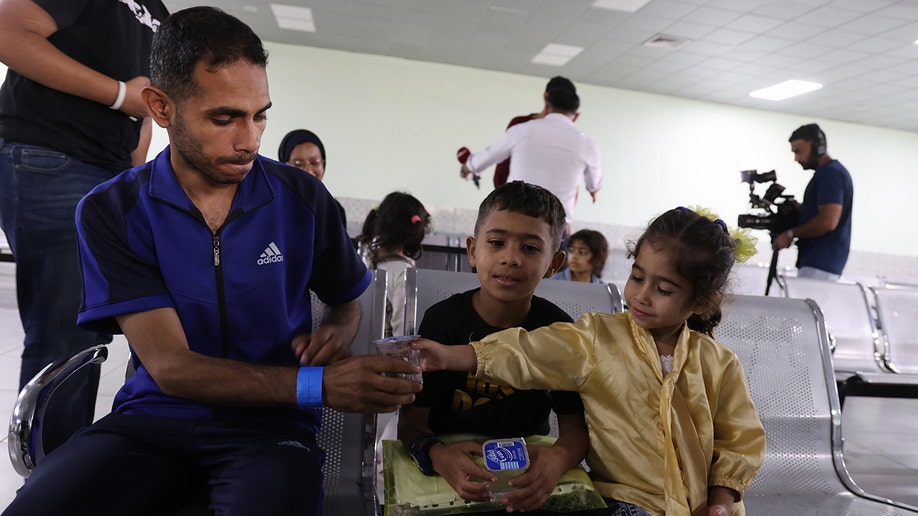 A man hands a child a snack in the Gaza Strip as they wait to be evacuated by the Jordan Armed Forces.