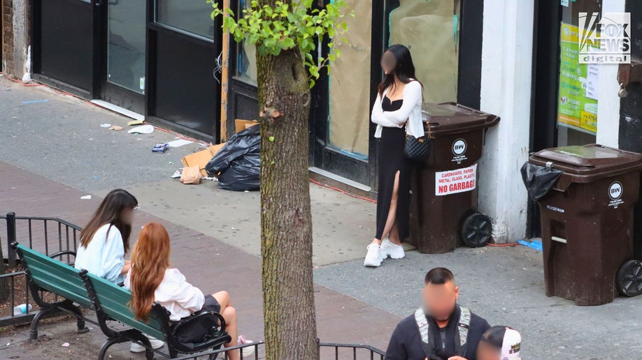 An alleged sex workers stands while two other alleged prostitutes sit on a bench in Queens.