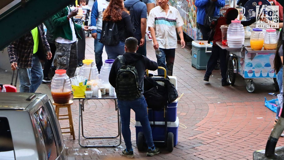 A man selling drinks under the subway tracks on Roosevelt Avenue in Queens, New York City.