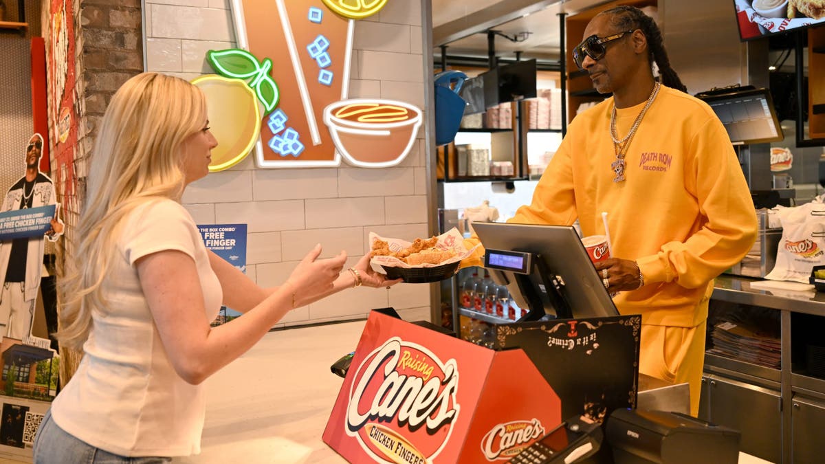 snoop dogg serves a customer behind the counter at raising cane's 
