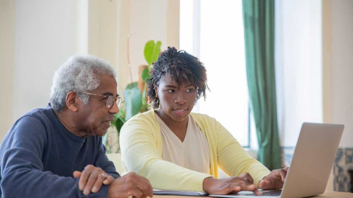 An elderly parent and his daughter looking at a laptop screen.