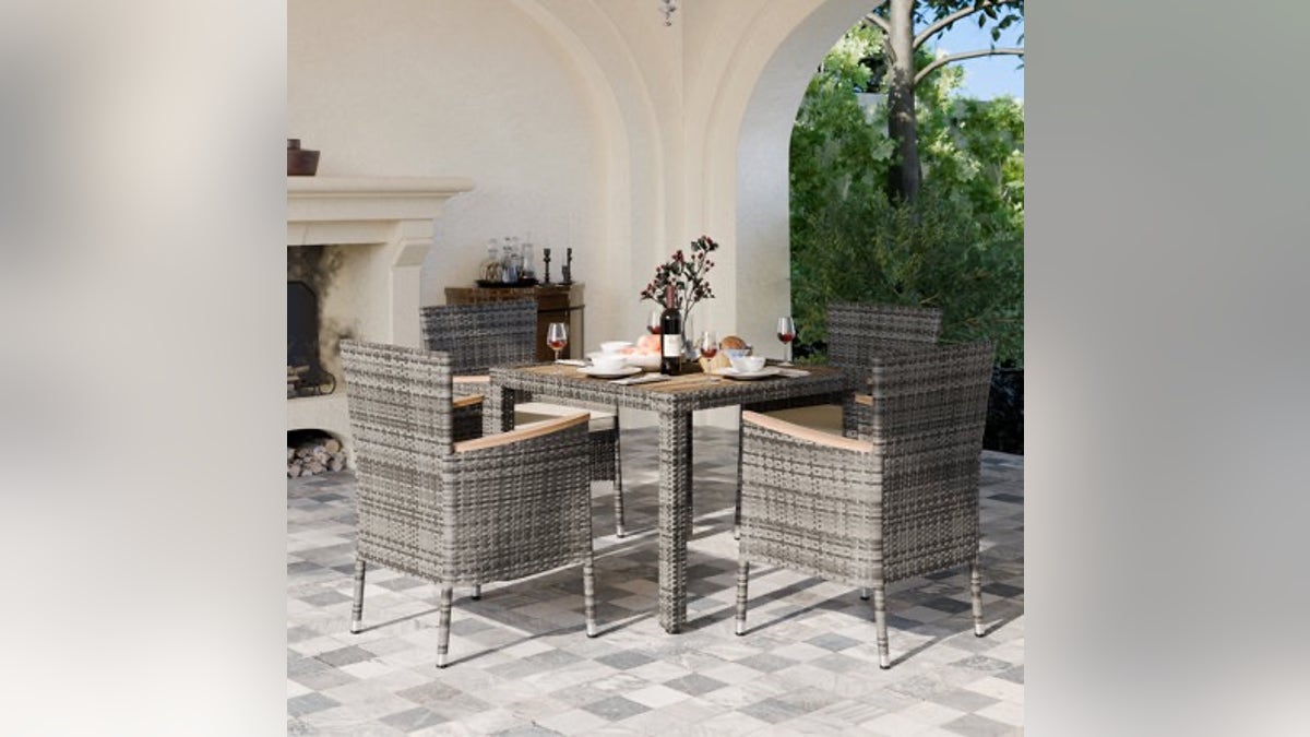 This sleek outdoor dining set comes complete with a solid wood table plus four stackable wicker chairs and cushions.