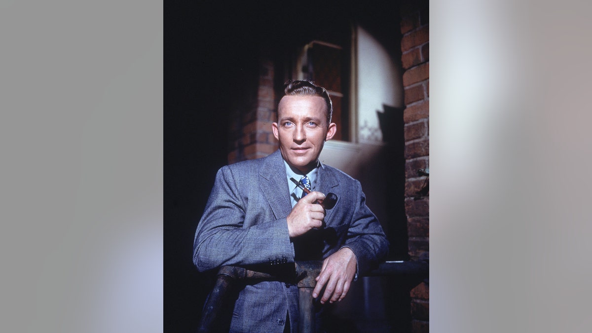 Bing Crosby in a blue suit posing with a smoking pipe.