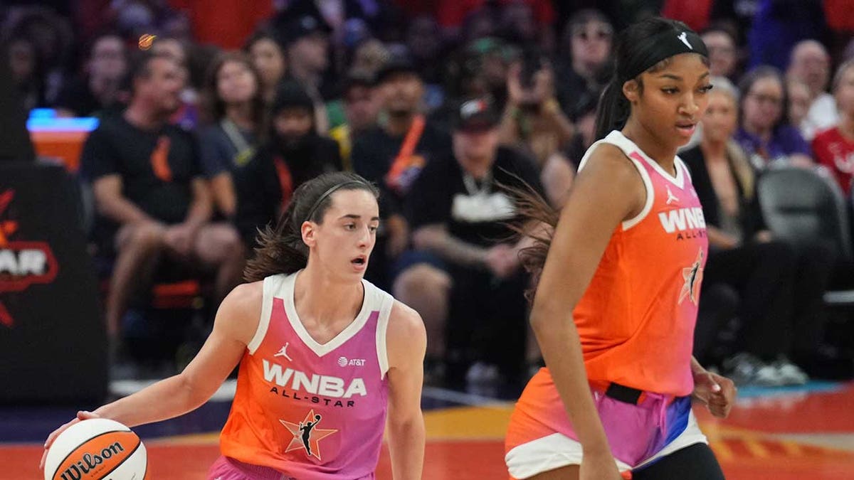 Caitlin Clark dribbles alongside Angel Reese