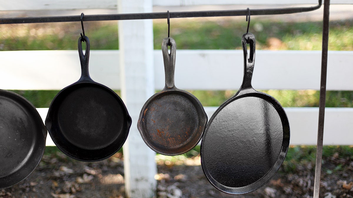 Four cast-iron skillets hang outside in front of a white fence.