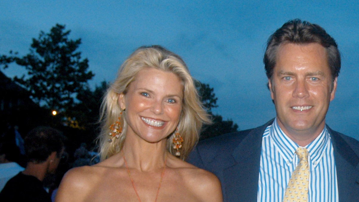 Christie Brinkley sonriendo junto a Peter Cool con un traje azul y una corbata amarilla.