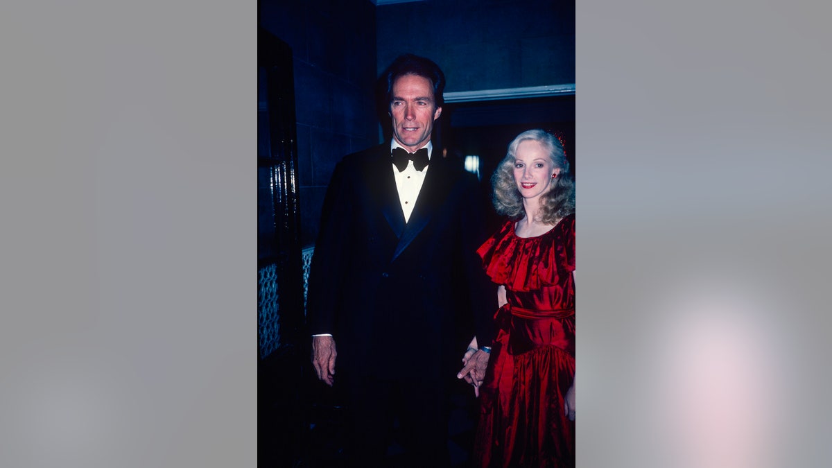 Clint Eastwood in a tux walking alongside Sondra Locke wearing a bright red dress.
