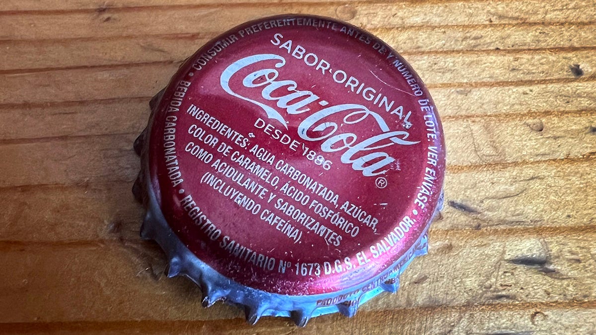Cap from glass Bottle of Coca-Cola made in Mexico seen on wood table, ingredients seen in Spanish
