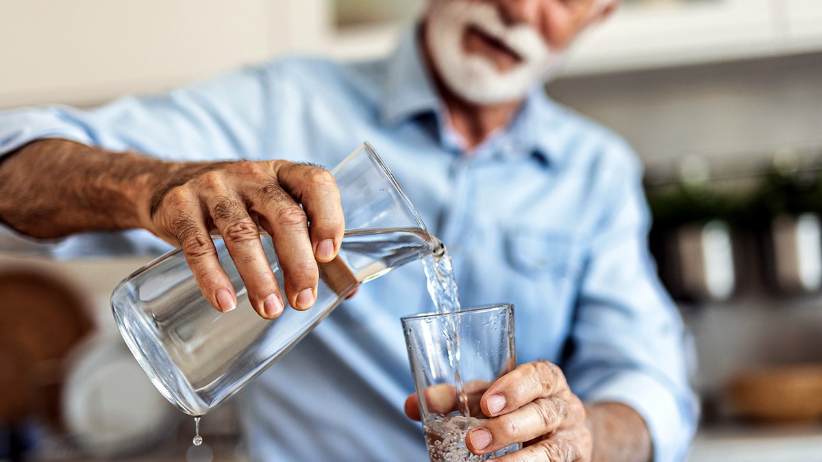 Senior man pouring water from the jug into glass in the kitchen.