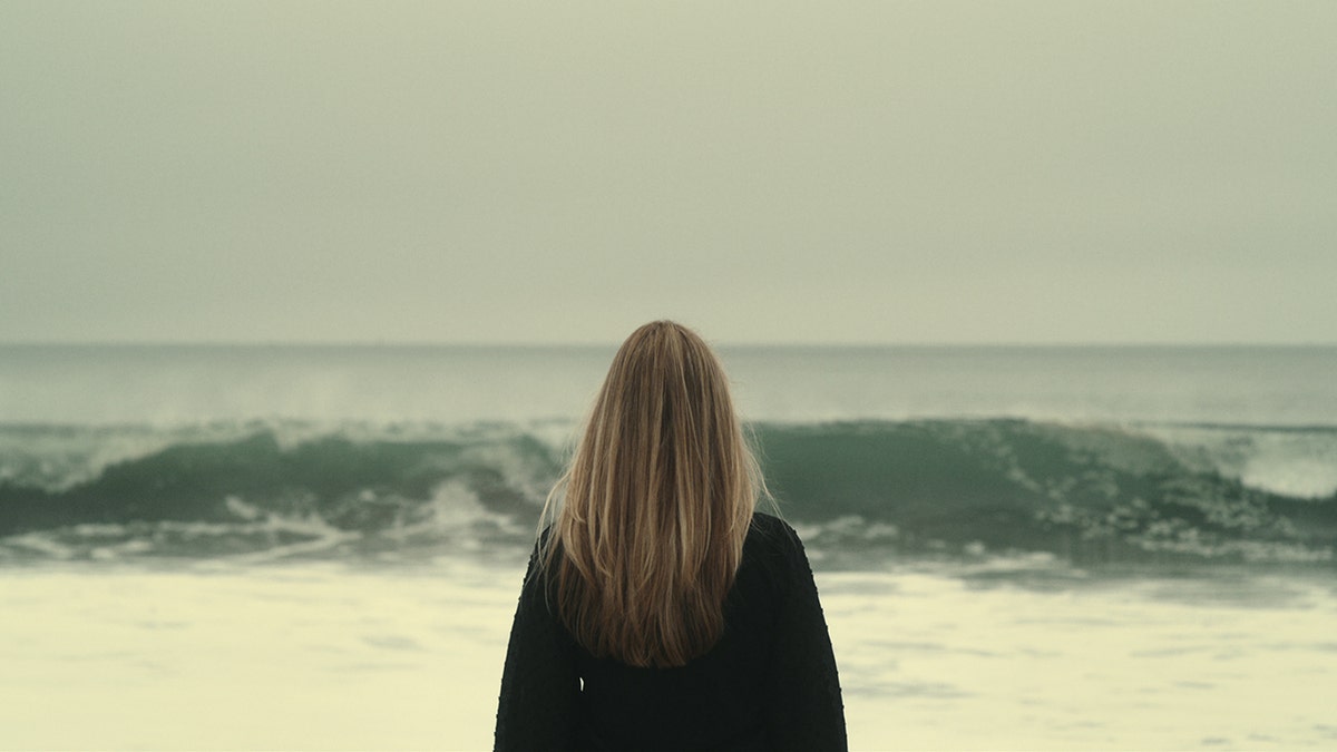 Denise Huskins with her back turned looking at the ocean.