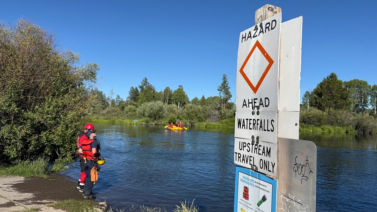 Buscar y rescatadores de pie a lo largo del río cerca del signo de peligro