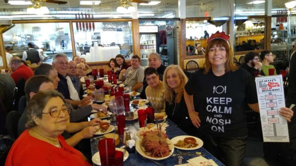 Ellen Fried poses for a photograph at a table of other pastrami lovers while holding a menu for Harold's New York Deli.