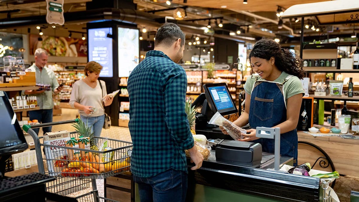 Happy African American cashier working at the supermarket registering products and talking to a customer