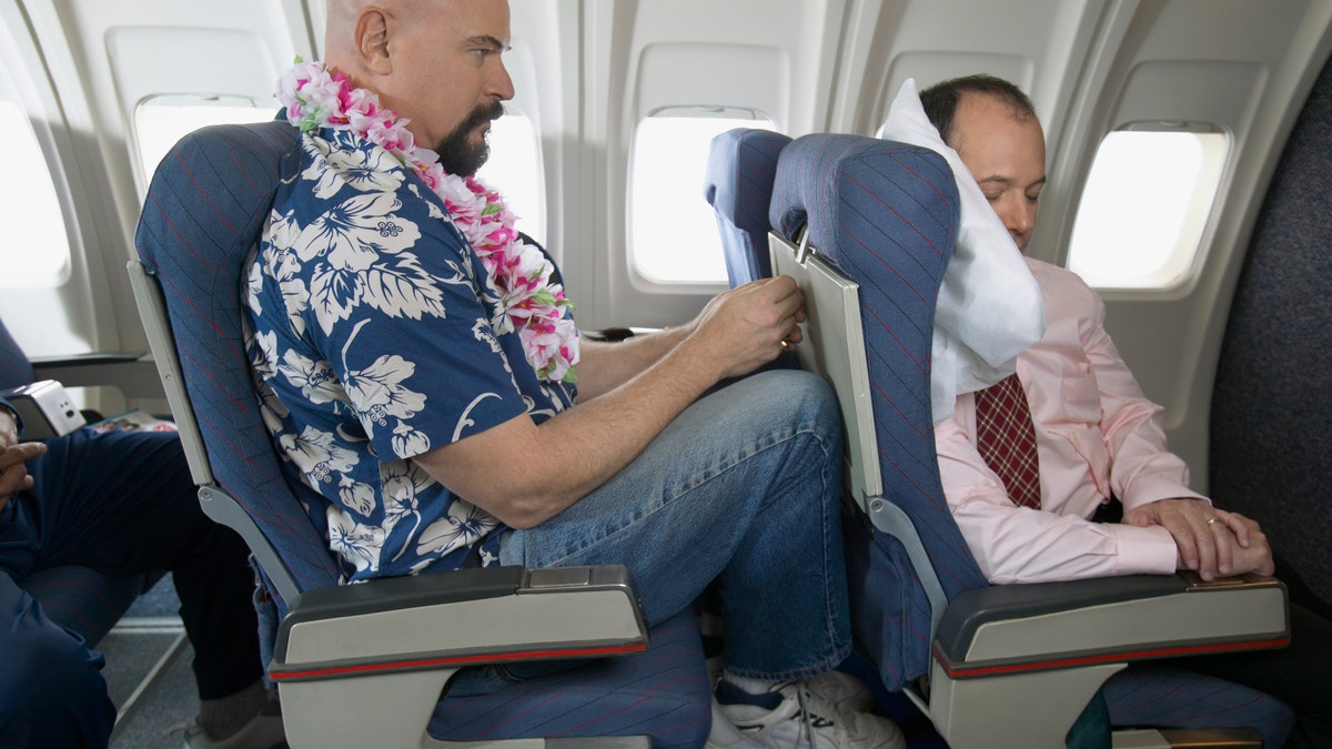 Passenger With His Knees Against a Sleeping Businessman's Chair on an Aeroplane