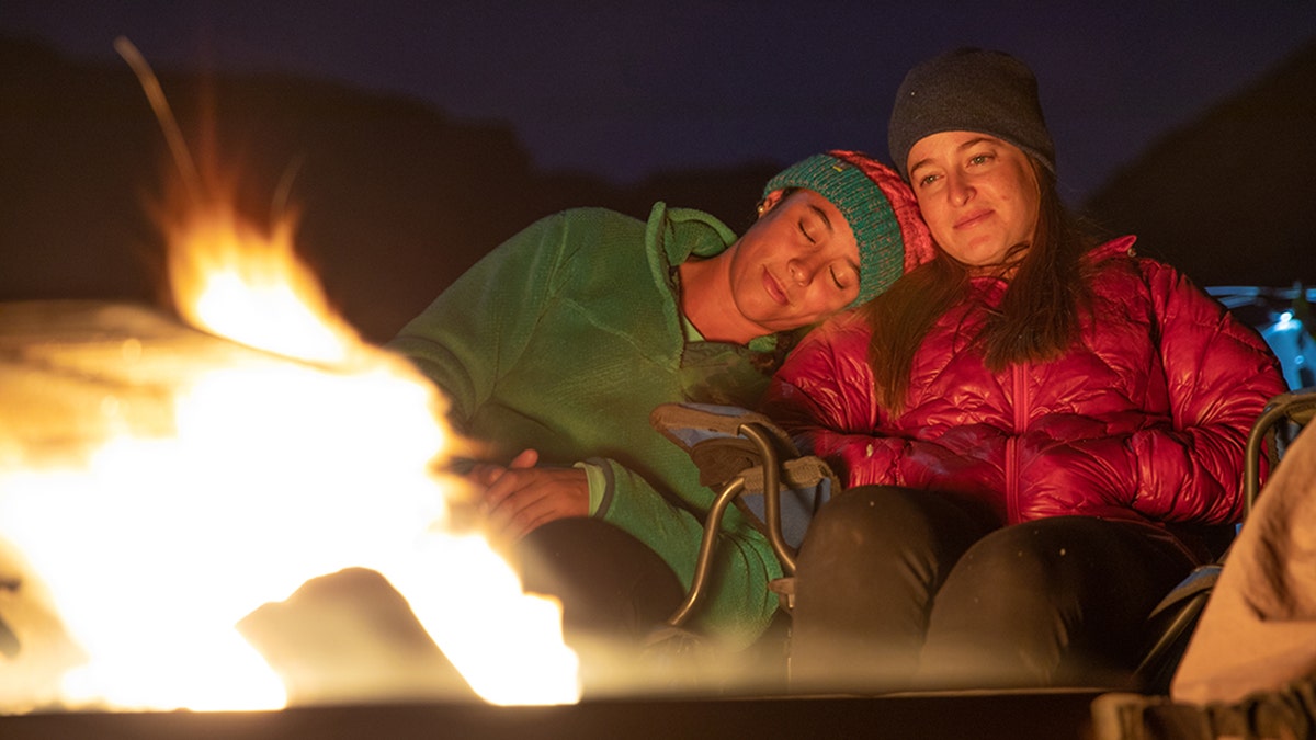 two women sit close to eachother in front of a fire