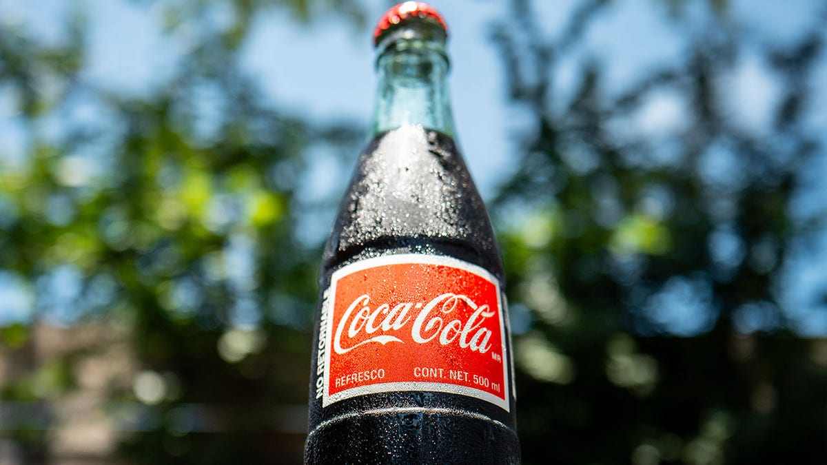 Glass bottle of Coca-Cola made in Mexico seen with Spanish label and background of trees in Texas