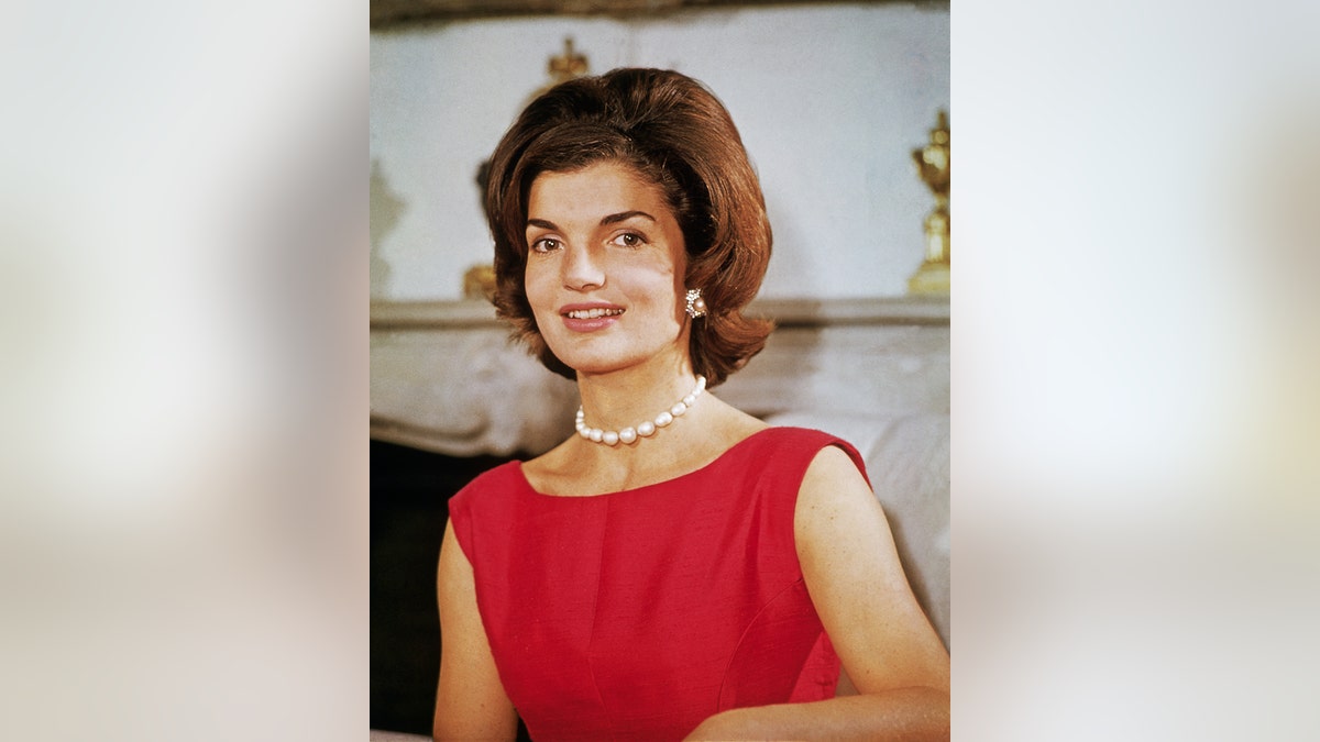 Jackie Kennedy wearing a sleeveless red dress with pearls.