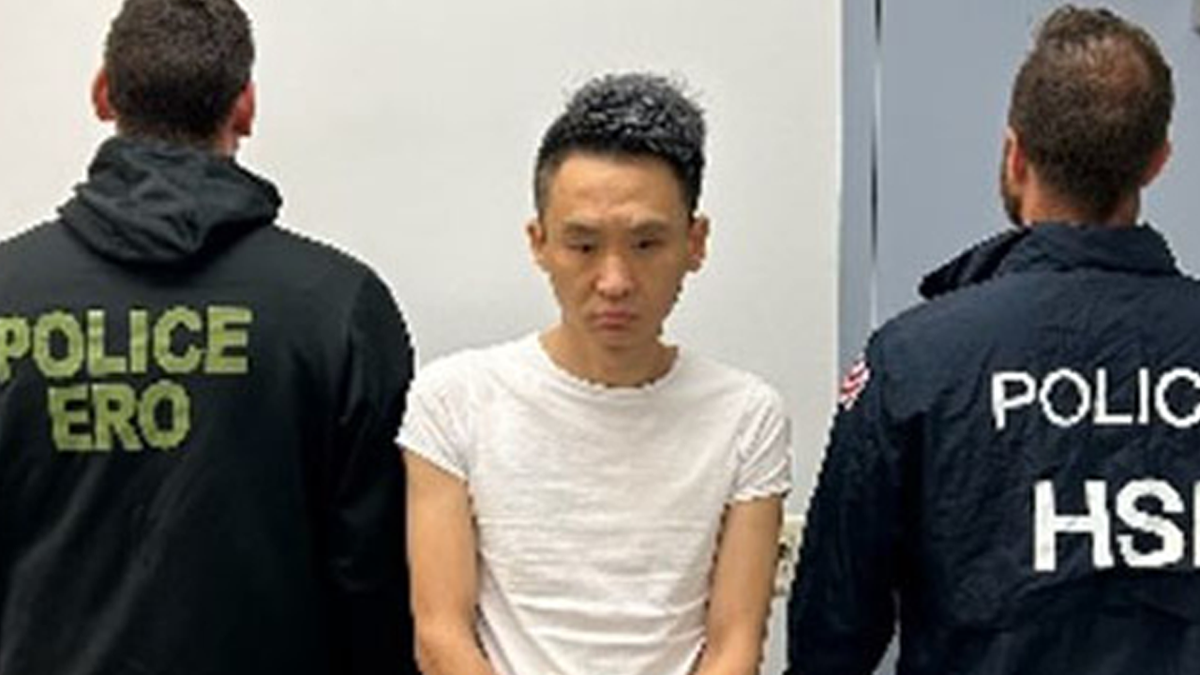 Jian Chen in a white T-shirt flanked by two federal agents with their backs turned