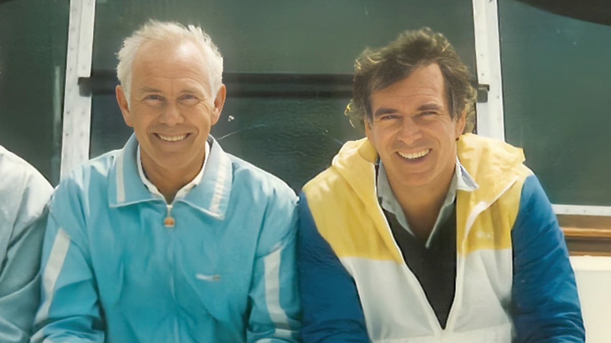 Johnny Carson con una chaqueta azul sentada al lado de Howard Smith con una chaqueta azul, blanca y amarilla mientras ambos sonríen.