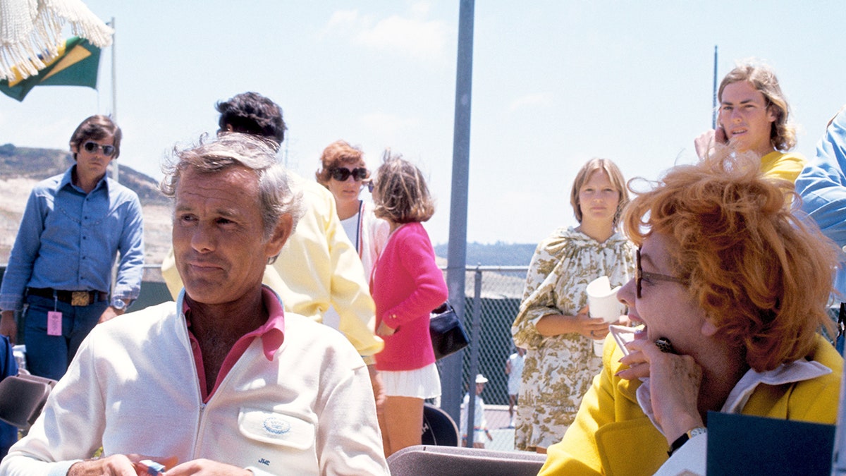 Johnny Carson con una camisa blanca sentada al lado de Lucille Ball con una chaqueta amarilla.