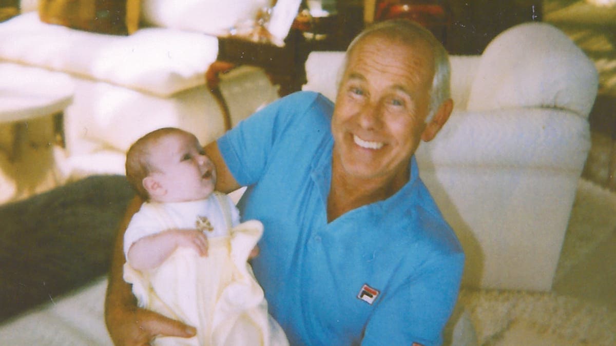 Johnny Carson con una camisa azul brillante sosteniendo un bebé.