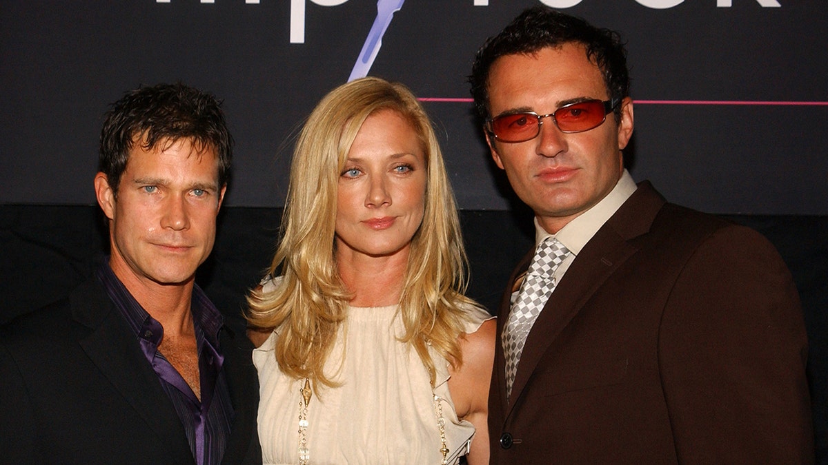The cast of "Nip/Tuck" leaning against each other closely looking serious.