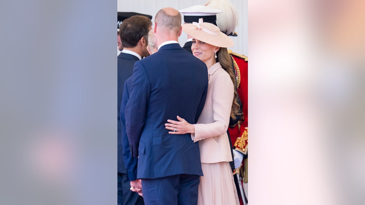 Kate Middleton holding connected to Prince William who is wearing a bluish suit arsenic she wears a ray pinkish overgarment dress.