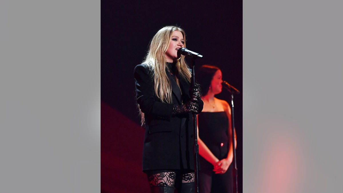 Kelly Clarkson wearing all black singing on stage.