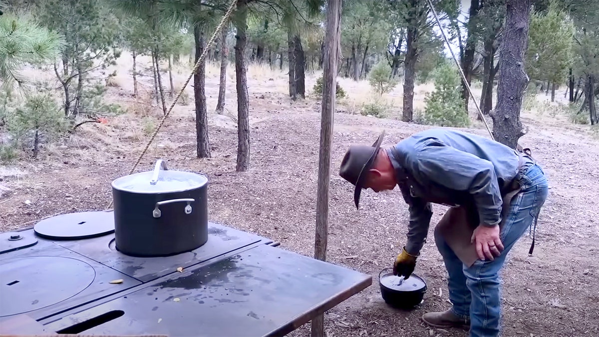 Kent Rollins bends over to pick up a cast-iron dutch oven.