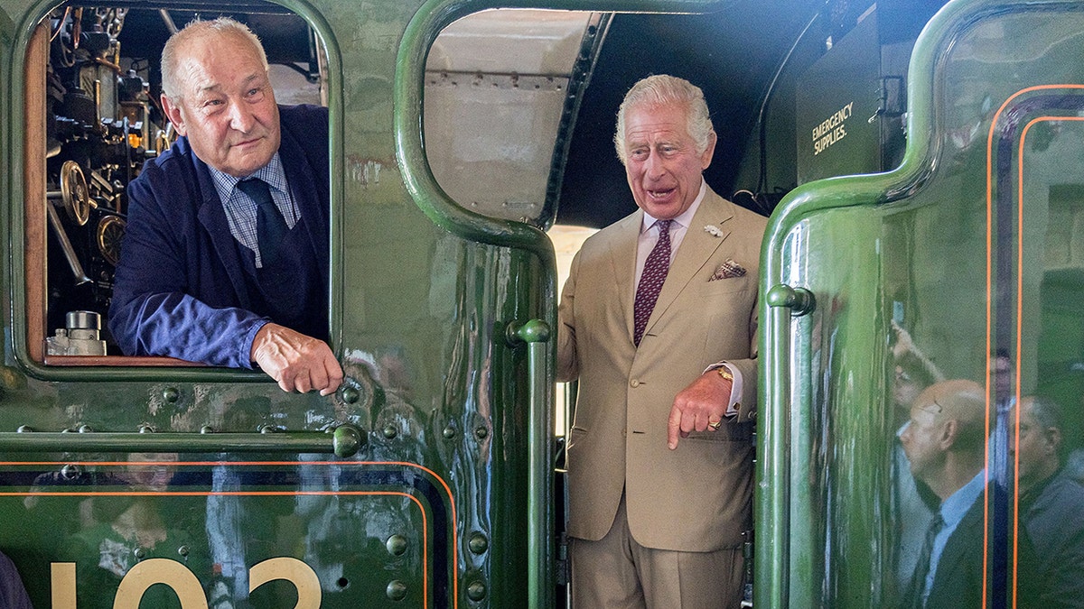 King Charles in a beige suit inside a green train.