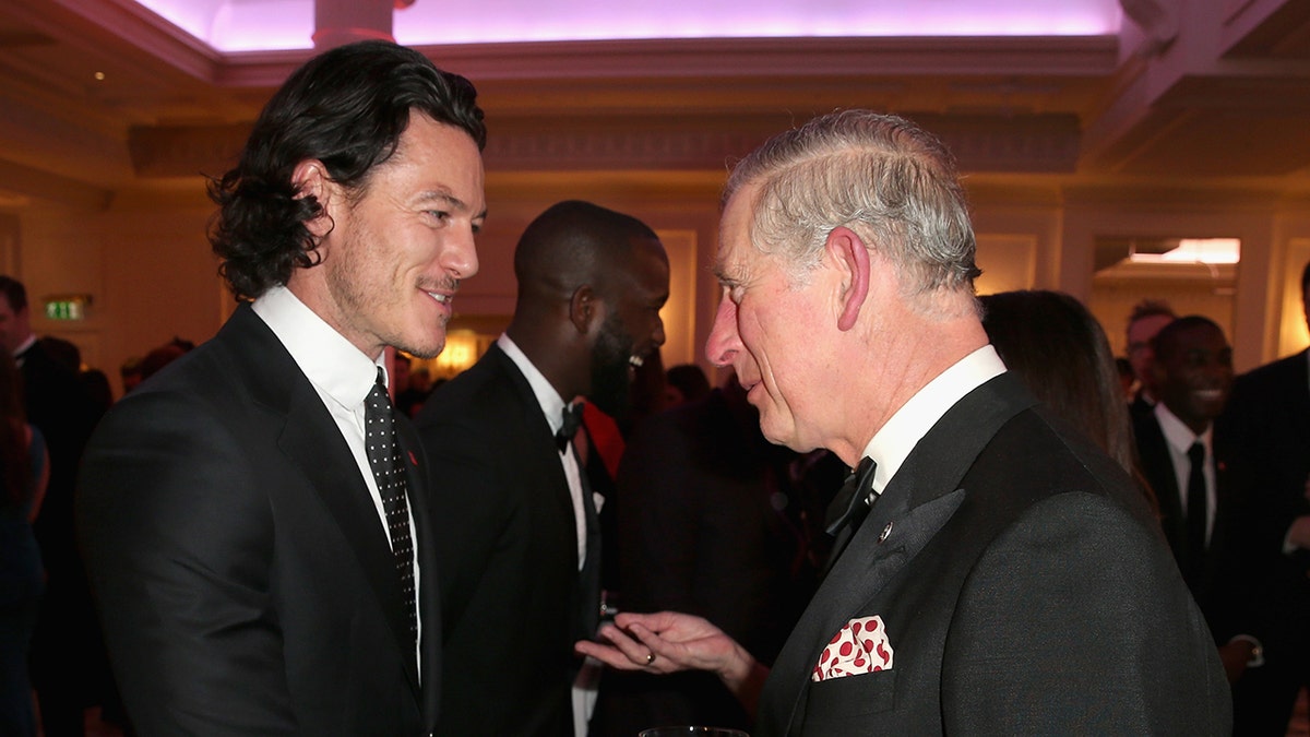 Luke Evans in a suit greeting King Charles.