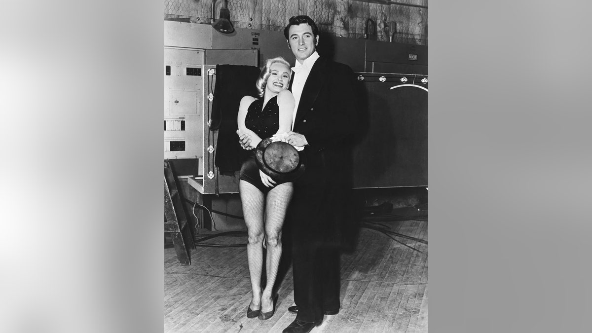 Mamie Van Doren smiling in a black halter dress being embraced by Rock Hudson in formal wear.