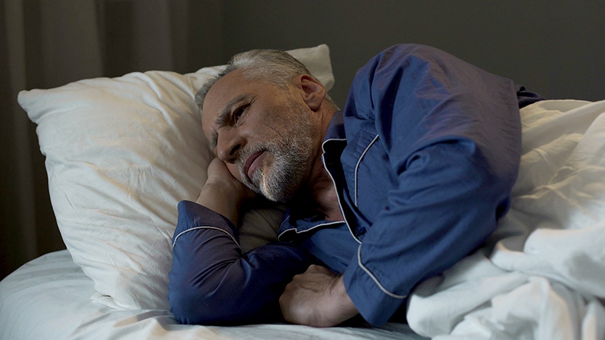 senior man attempting to fall asleep in bed