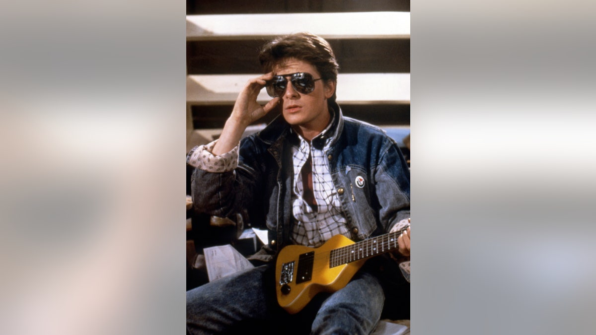 Michael J Fox adjusting his sunglasses and holding a guitar.
